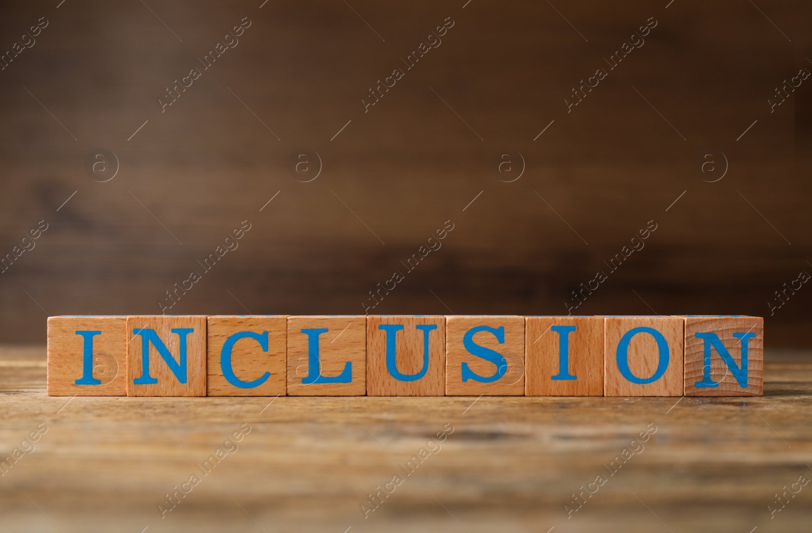 Photo of Many cubes with word Inclusion on wooden table against blurred background. Space for text