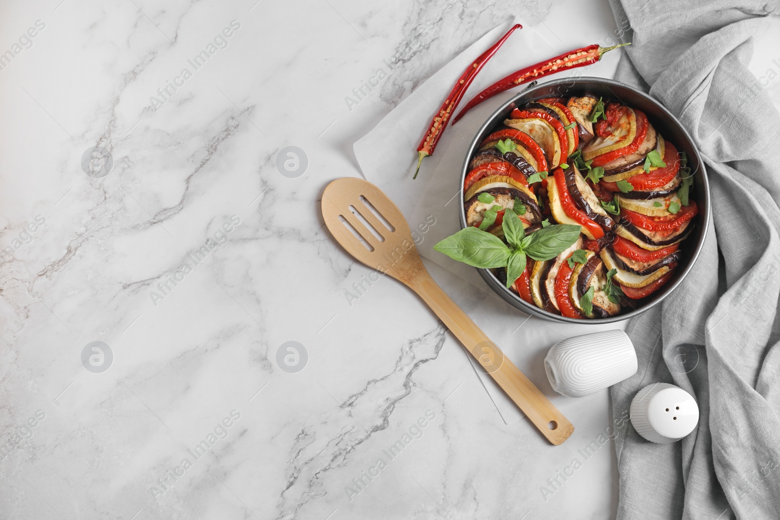 Photo of Delicious ratatouille, chili peppers and spatula on white marble table, flat lay. Space for text