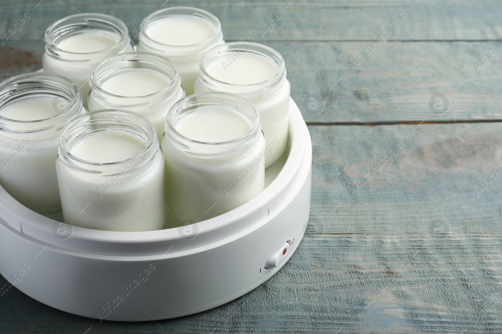 Photo of Modern yogurt maker with full jars on blue wooden table. Space for text