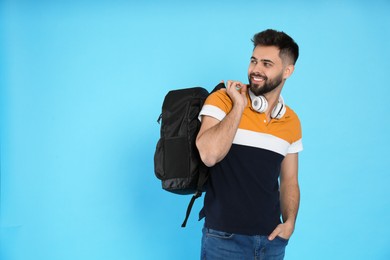 Young man with stylish backpack and headphones on light blue background. Space for text