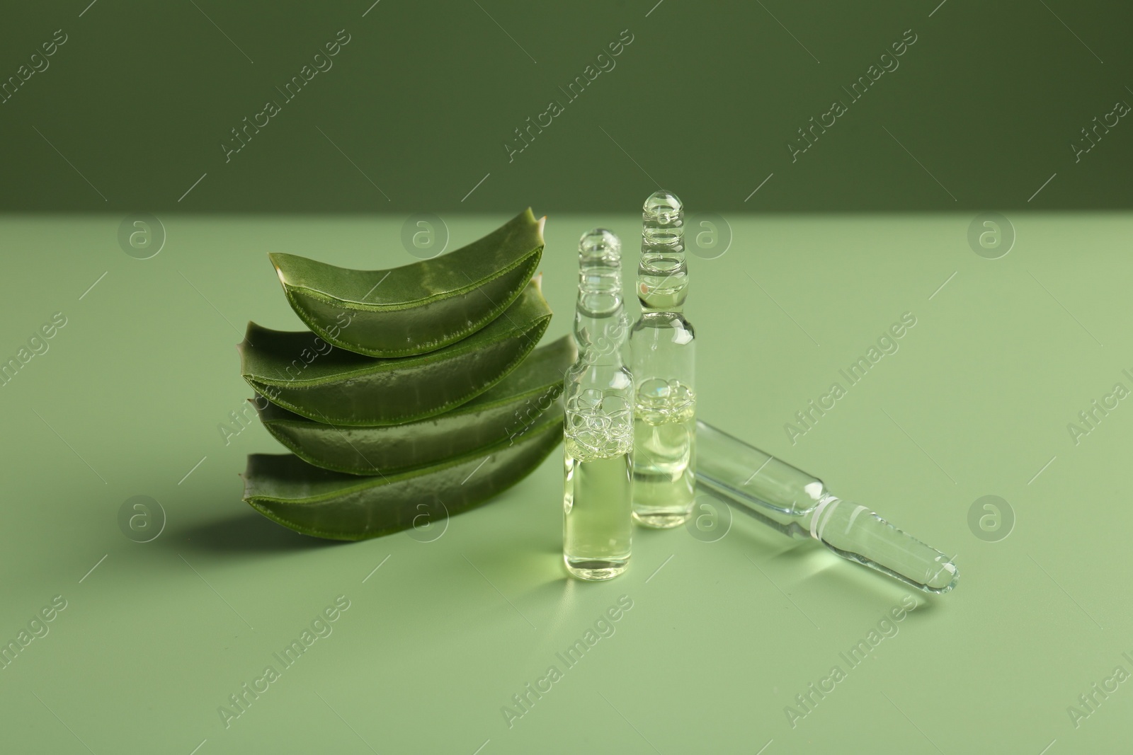 Photo of Skincare ampoules with extract of aloe vera and cut green leaves on color background