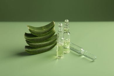 Skincare ampoules with extract of aloe vera and cut green leaves on color background