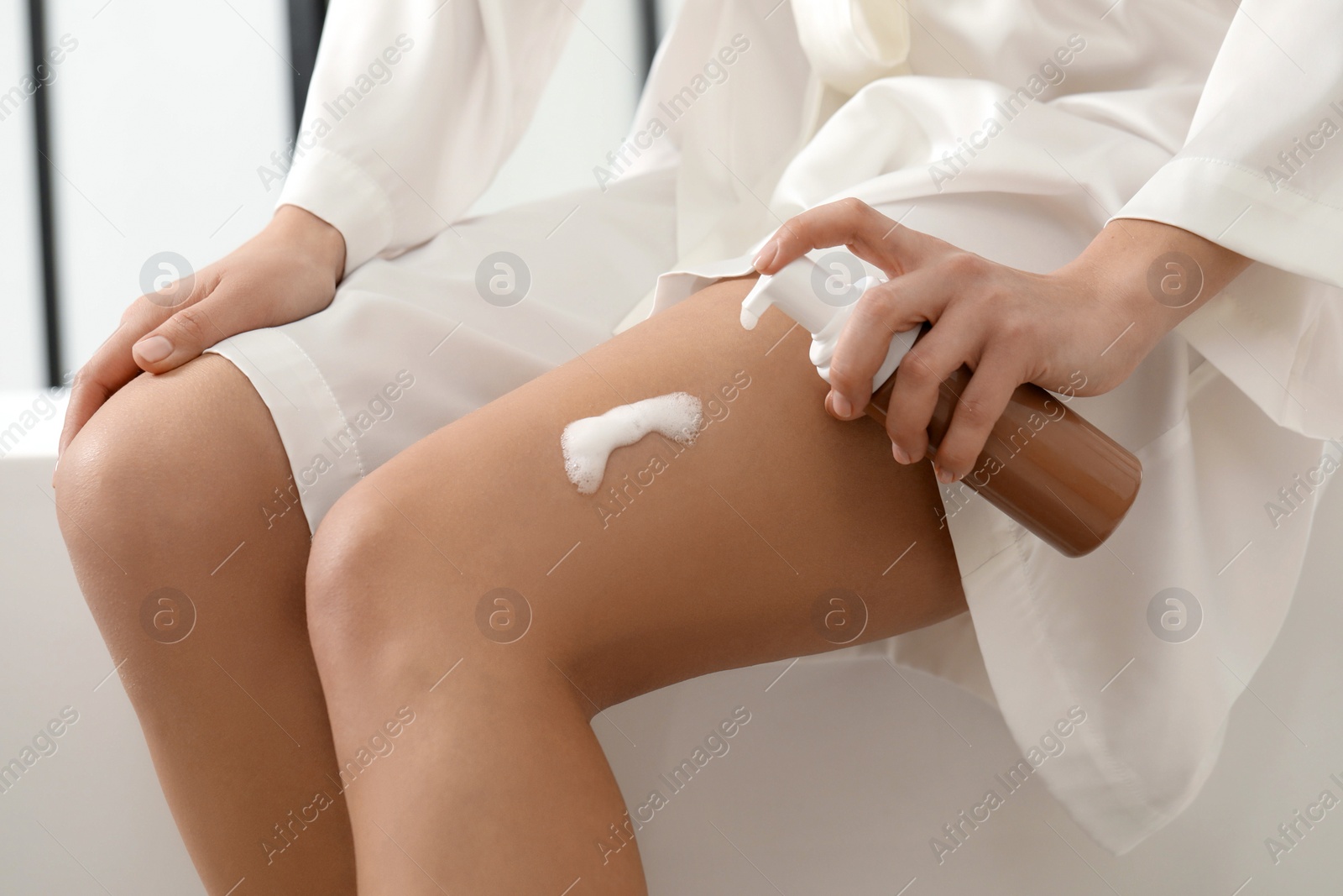 Photo of Woman applying self-tanning product onto leg indoors, closeup