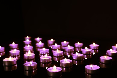 Beautiful burning violet candles on black background. Funeral attributes