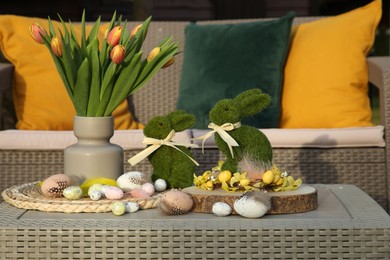 Photo of Terrace with Easter decorations. Bouquet of tulips in vase, bunny figures and decorative eggs on table outdoors