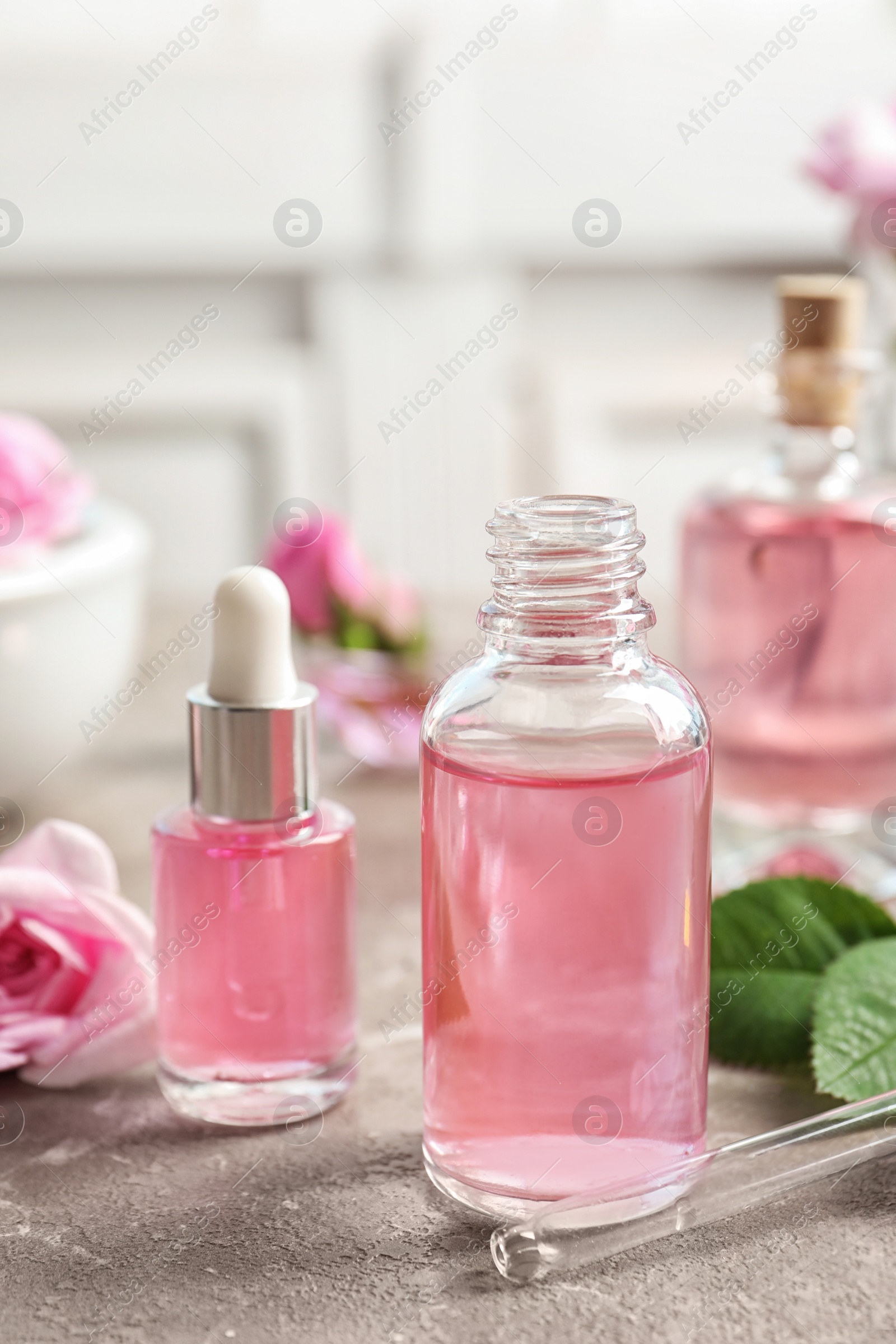 Photo of Bottles of rose essential oil, pipette and flowers on table, space for text