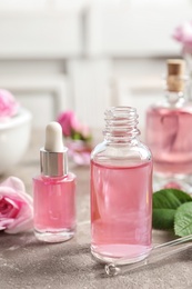 Photo of Bottles of rose essential oil, pipette and flowers on table, space for text