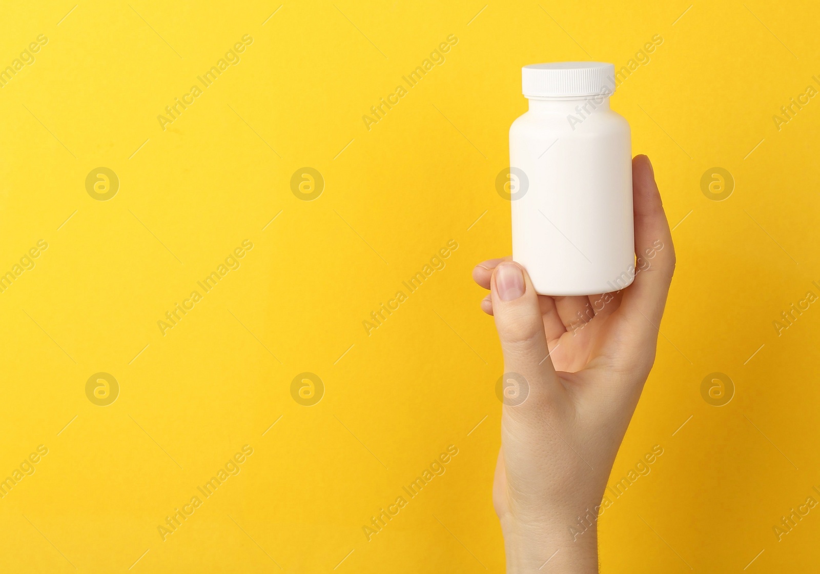 Photo of Woman holding blank white jar of vitamins on yellow background, closeup. Space for text