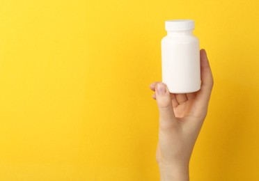 Photo of Woman holding blank white jar of vitamins on yellow background, closeup. Space for text