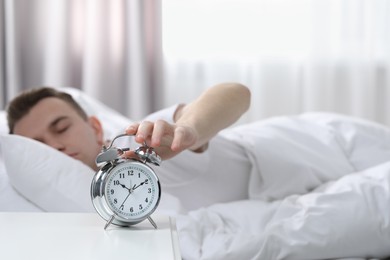Photo of Sleepy man turning off alarm clock at home in morning, focus on hand. Space for text