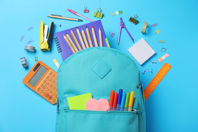 Photo of Stylish backpack with different school stationery on light blue background, flat lay