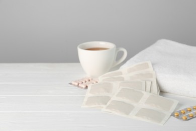Photo of Mustard plasters, pills, towel and tea on white wooden table, space for text