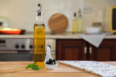 Photo of Bottle of cooking oil, olives and basil on wooden table in kitchen, space for text