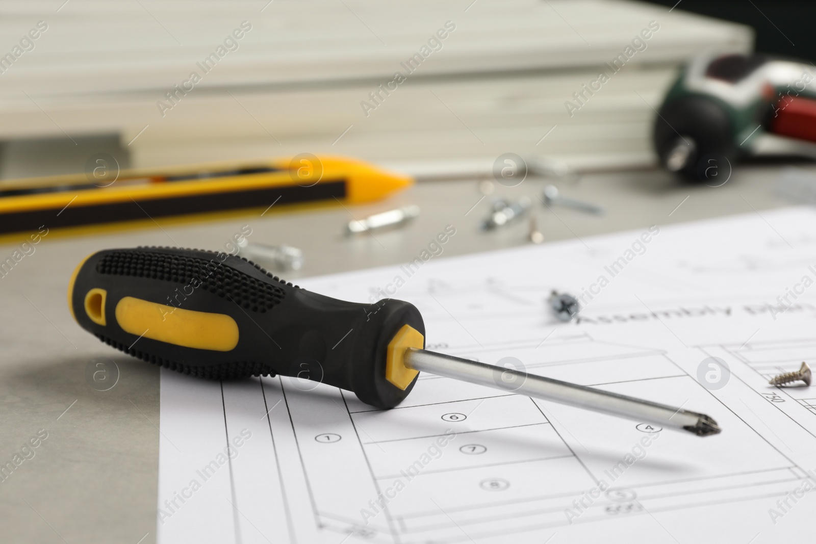 Photo of Furniture assembly plan, screwdriver and different fasteners on light grey table, closeup