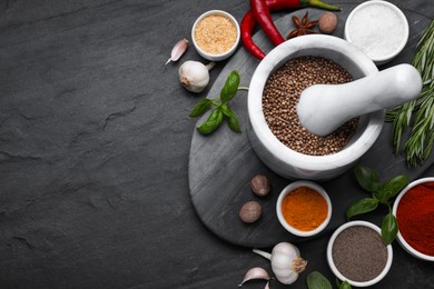 Photo of Mortar with pestle and different spices on black table, flat lay. Space for text