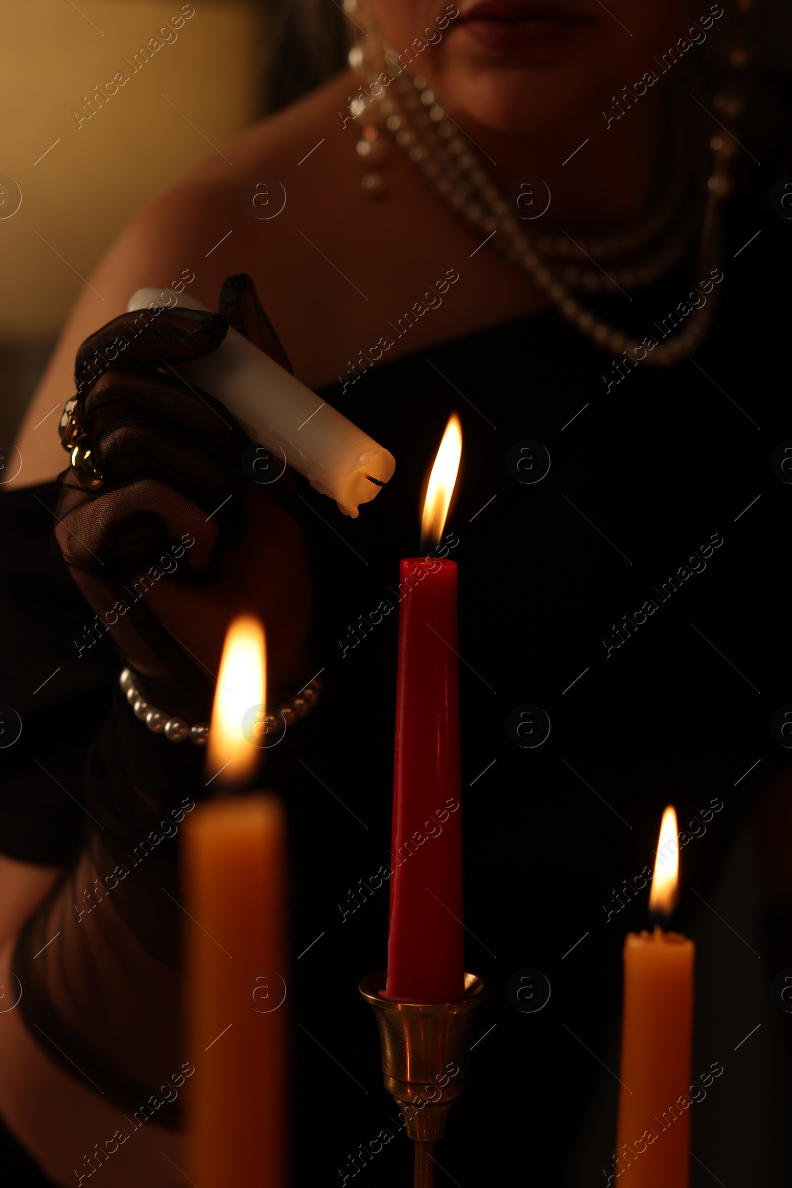 Photo of Woman with elegant jewelry lightning up candle indoors, closeup