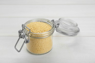 Glass jar of raw couscous on white wooden table, closeup