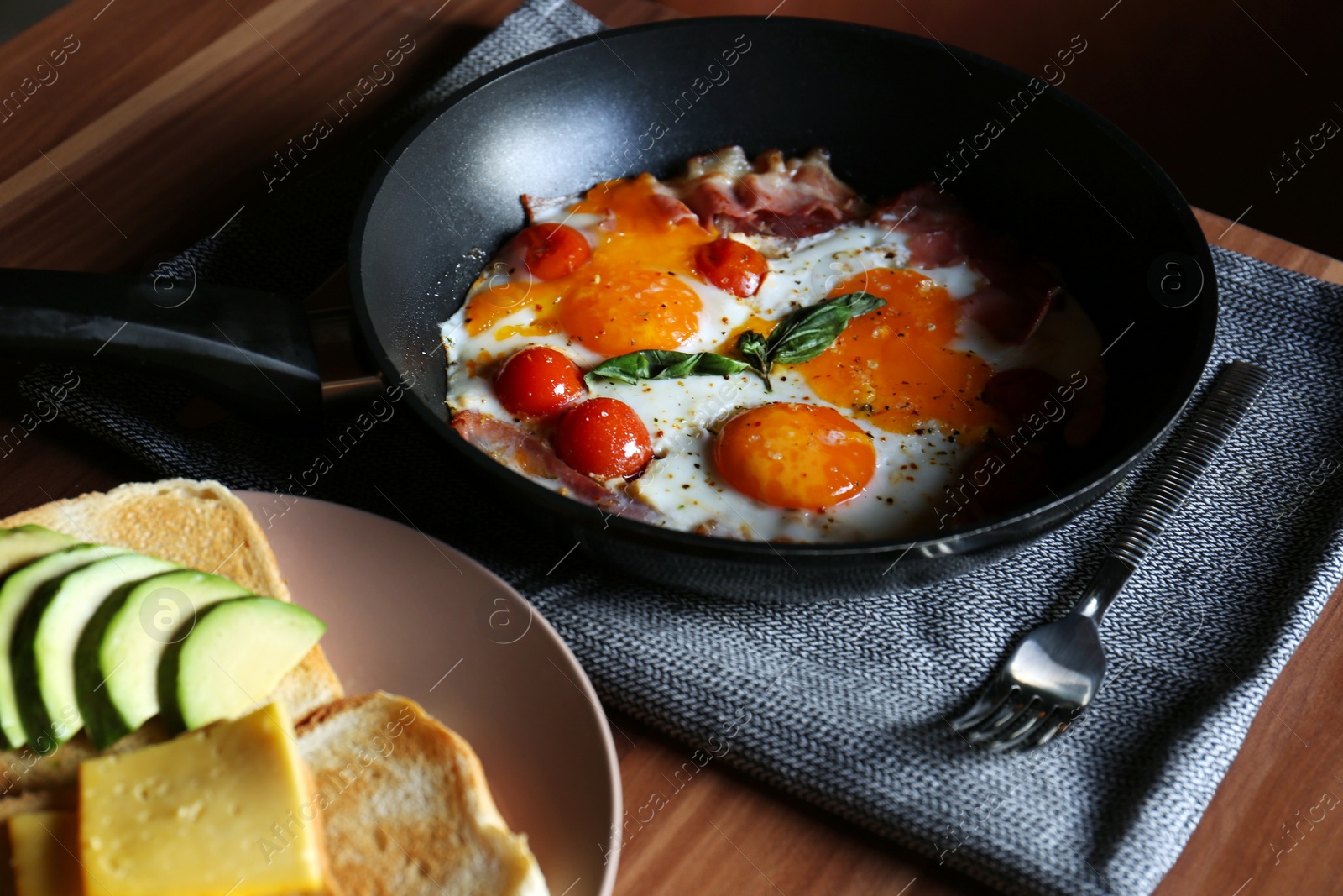 Photo of Fried eggs with bacon and tomatoes served with toasts on wooden table. Tasty breakfast