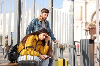 Being late. Worried couple with suitcases waiting at tram station outdoors, space for text