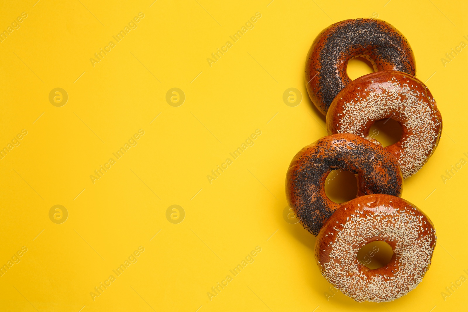 Photo of Many delicious fresh bagels on yellow background, flat lay. Space for text