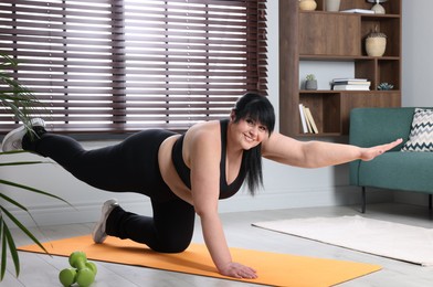 Photo of Overweight mature woman doing exercise on yoga mat at home