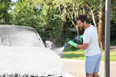 Photo of Man covering automobile with foam at outdoor car wash