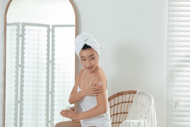 Photo of Beautiful young Asian woman applying body cream on shoulder in room