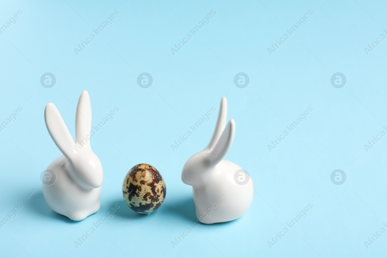 Photo of Ceramic Easter bunnies and egg on color background, space for text