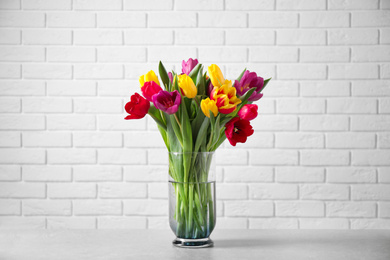 Photo of Beautiful spring tulips in vase on table near white brick wall