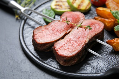 Board with slices of grilled meat on black table, closeup