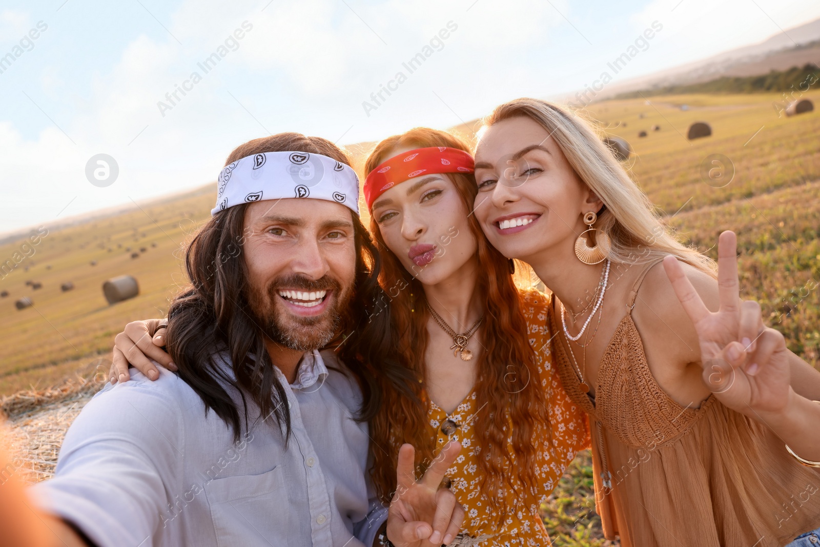 Photo of Happy hippie friends showing peace signs while taking selfie in field