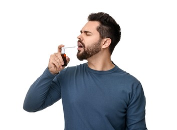 Young man using throat spray on white background