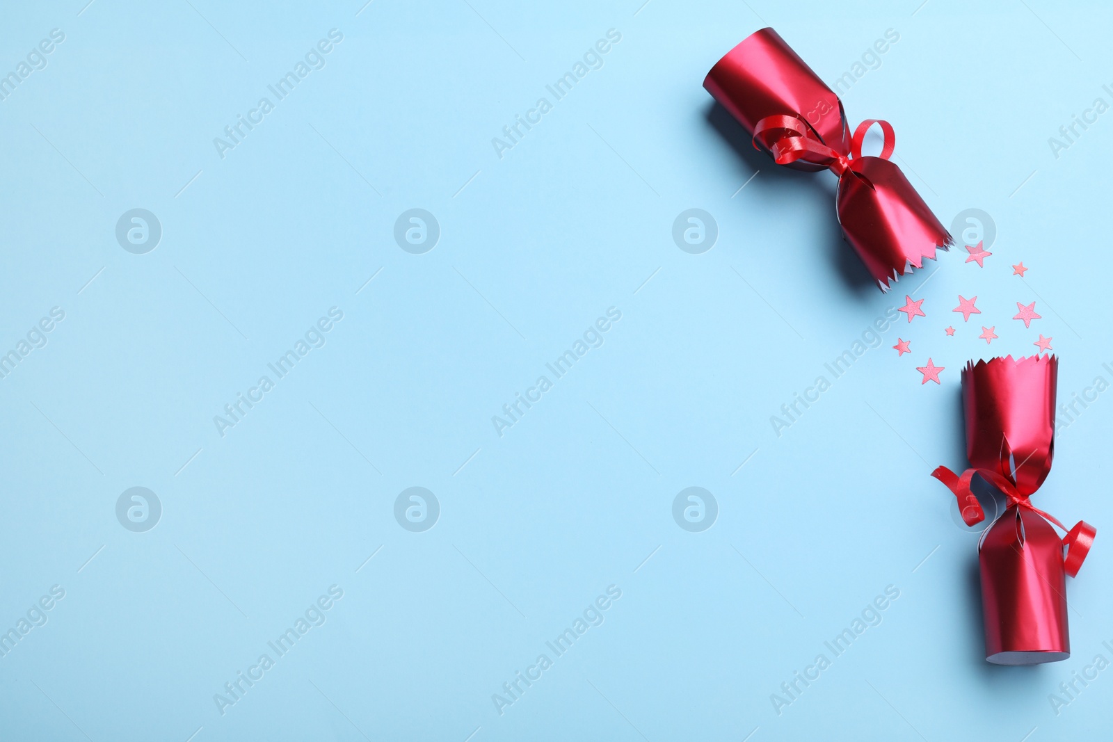 Photo of Open red Christmas cracker with shiny confetti on light blue background, top view. Space for text