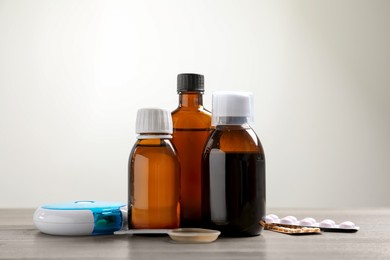 Photo of Bottle of syrup, dosing spoon and pills on table against light background. Cold medicine