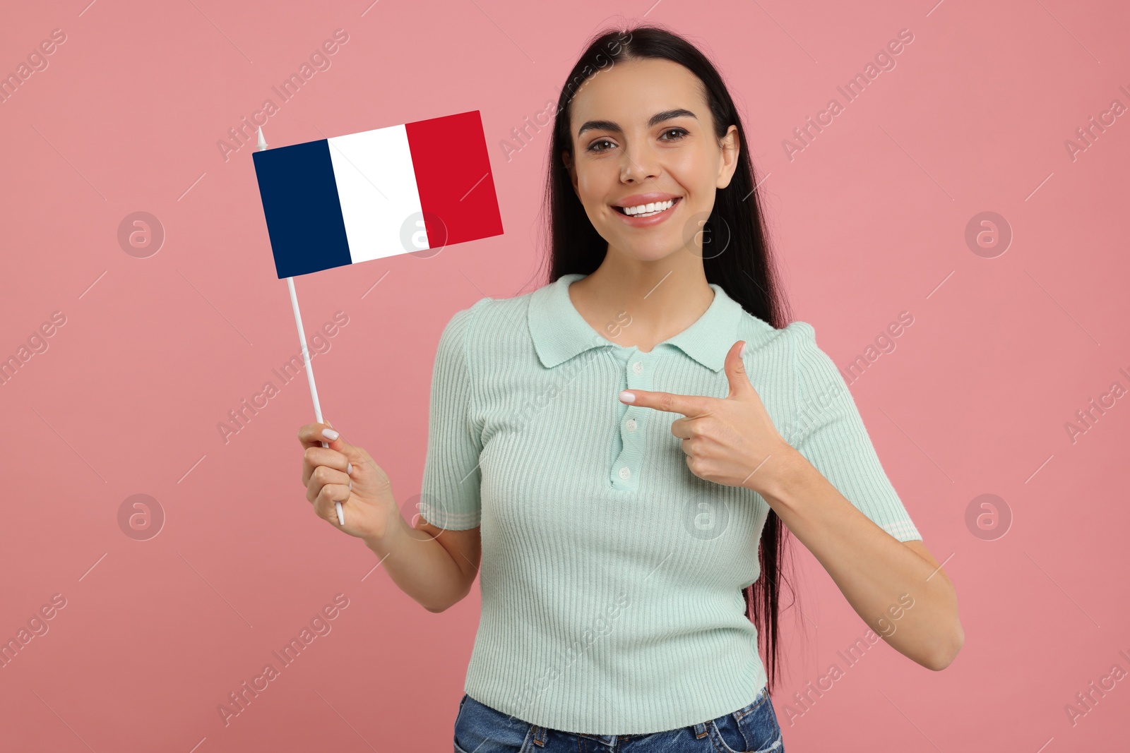 Image of Happy young woman pointing at flag of France on pink background