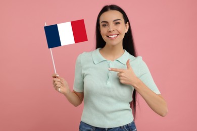 Happy young woman pointing at flag of France on pink background