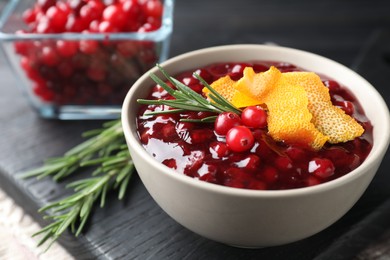 Photo of Fresh cranberry sauce, rosemary and orange peel in bowl on table, closeup