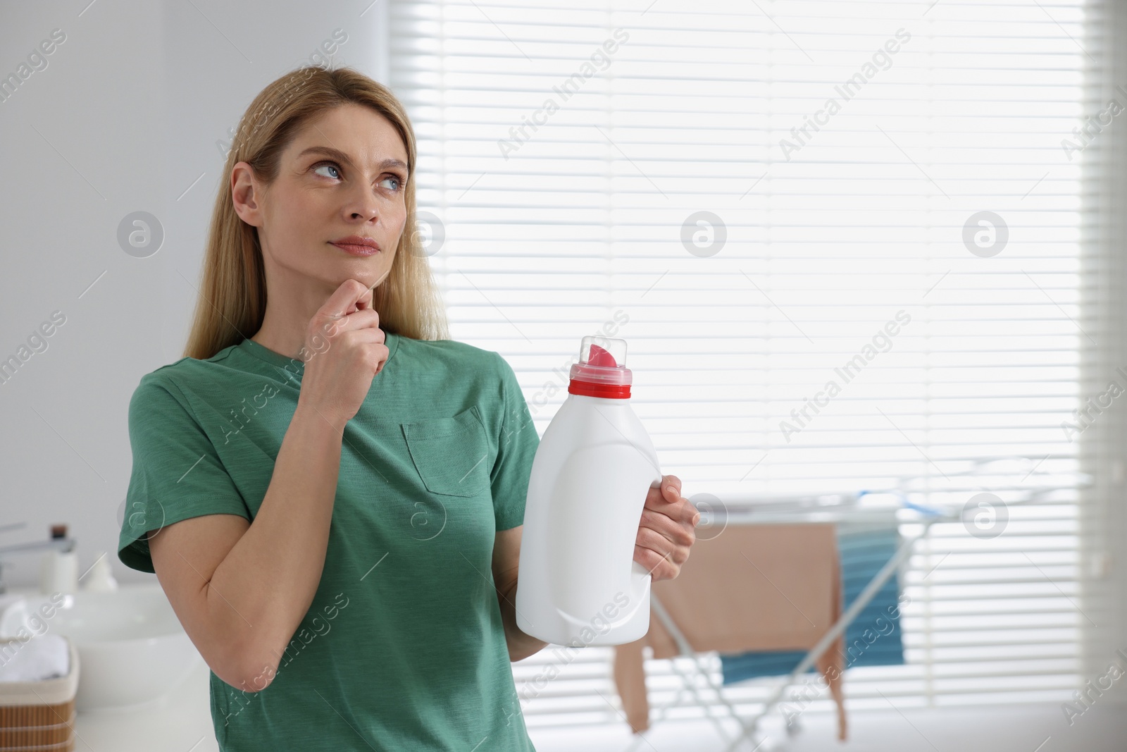 Photo of Thoughtful woman holding fabric softener in bathroom, space for text