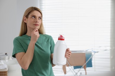Photo of Thoughtful woman holding fabric softener in bathroom, space for text