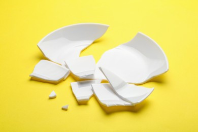 Photo of Pieces of broken ceramic plate on yellow background