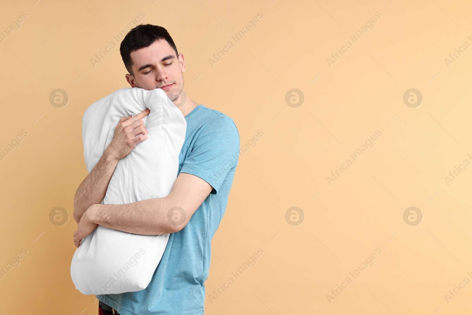 Photo of Man in pyjama holding pillow and sleeping on beige background, space for text