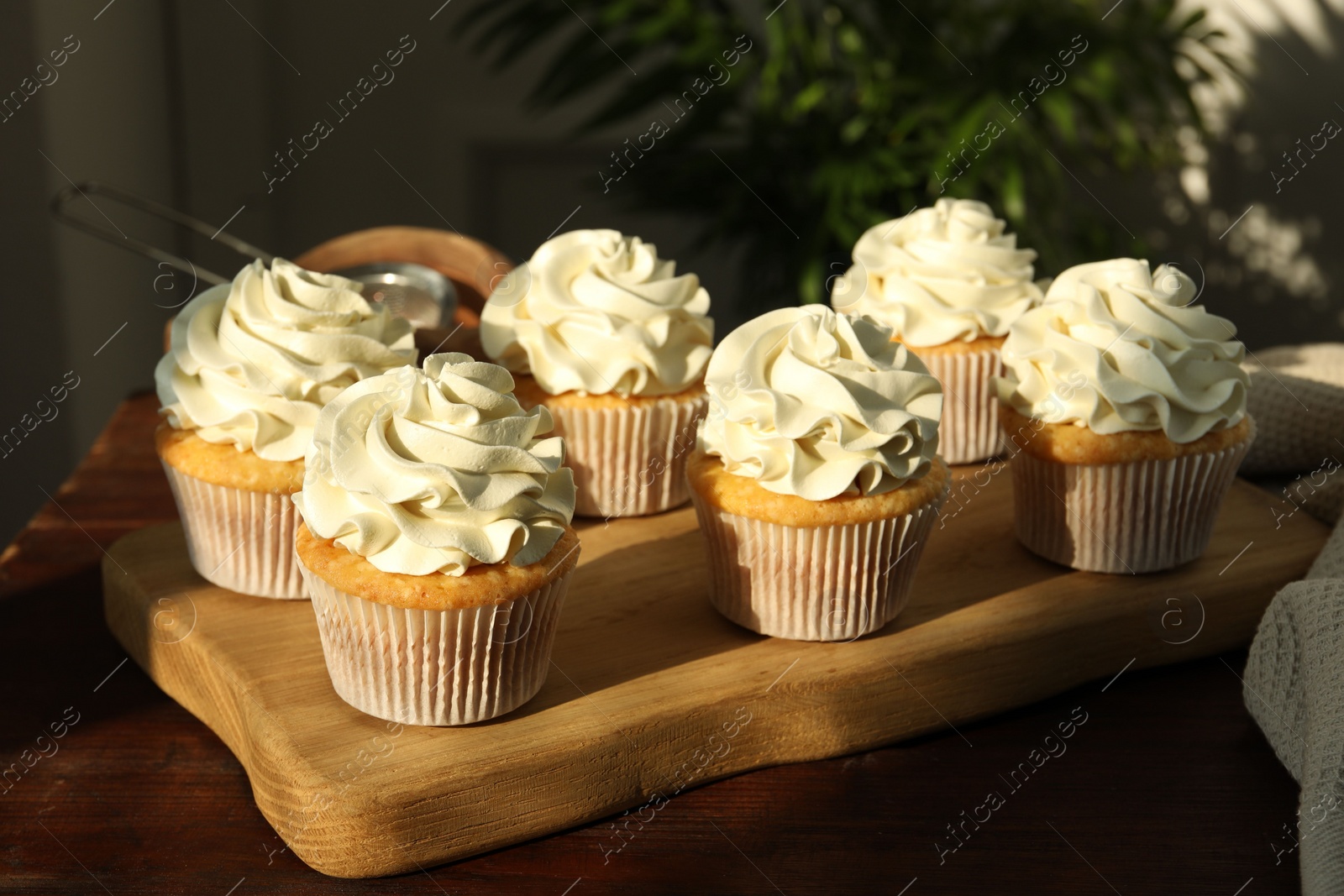 Photo of Tasty cupcakes with vanilla cream on wooden table, closeup