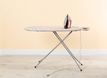 Photo of Board with modern iron near beige wall. Laundry day