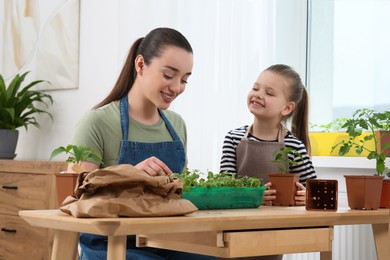 Photo of Mother and daughter planting seedlings into plastic container together at wooden table in room