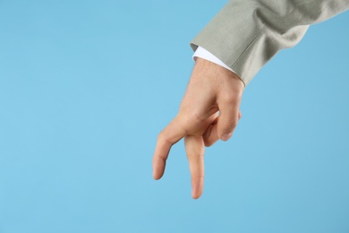 Photo of Businessman imitating walk with hand on light blue background, closeup. Finger gesture