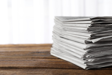 Stack of newspapers on wooden table, space for text. Journalist's work