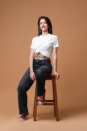 Smiling tattooed woman sitting on stool against beige background