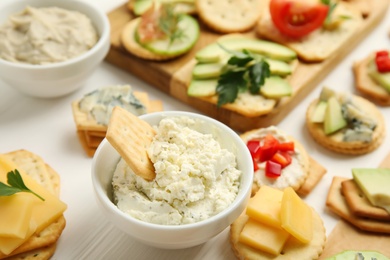 Different snacks with salted crackers on white wooden table, closeup