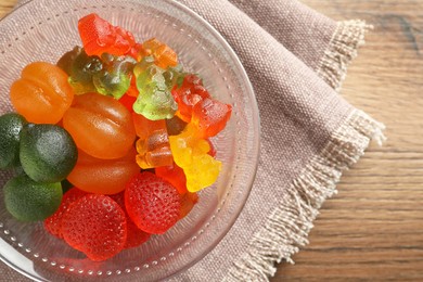 Different delicious gummy candies in glass bowl on wooden table, top view