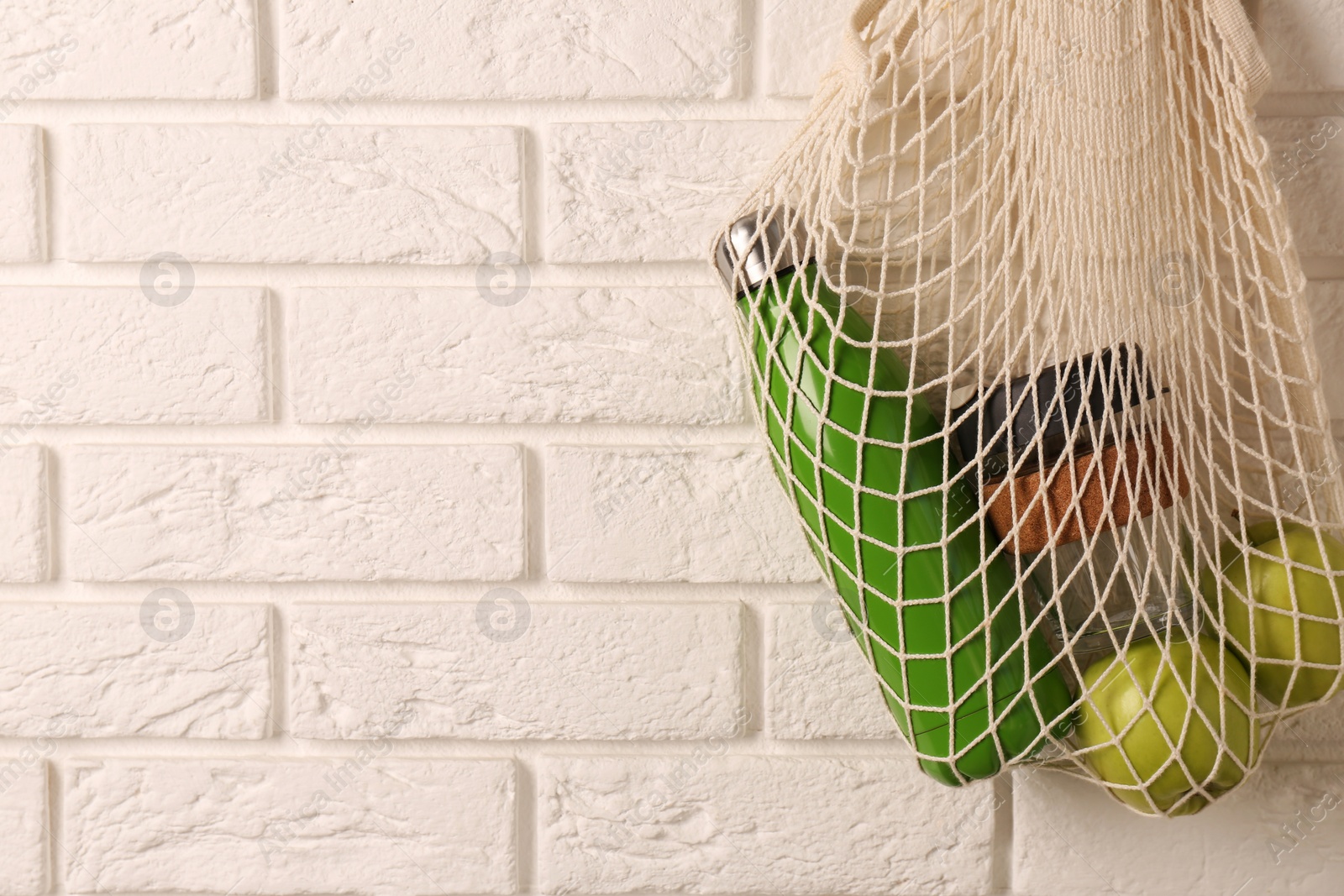 Photo of Net bag with different items hanging on brick wall, space for text. Conscious consumption